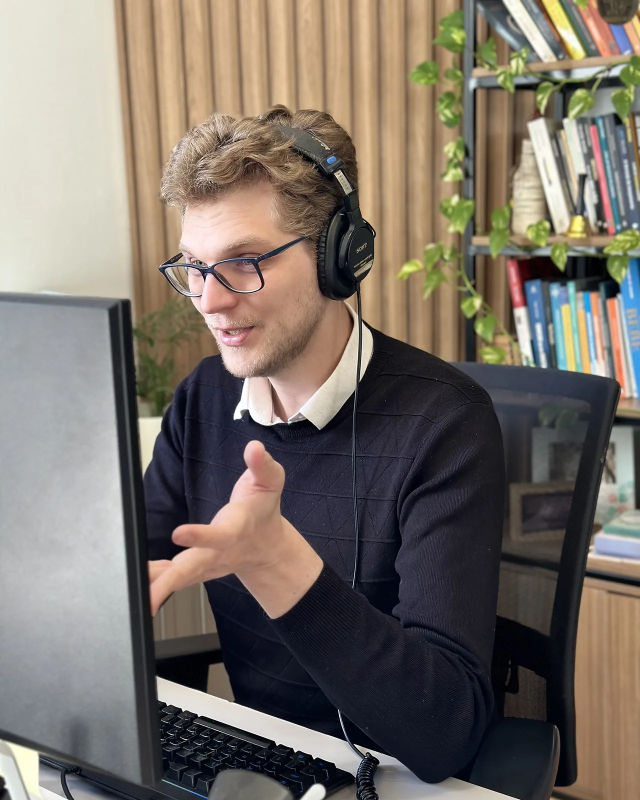 Ricardo Werlang de fone, no computador, estante de livros ao fundo.